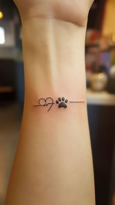 a small dog paw and heart tattoo on the left side of the wrist, with an arrow in the middle