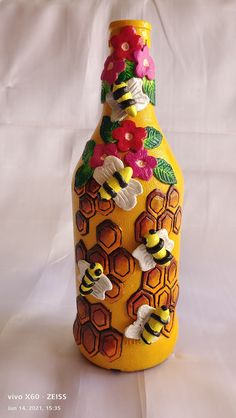 a yellow vase with flowers and bees painted on the bottom is sitting on a white surface