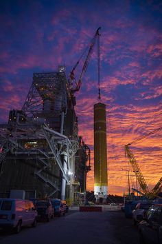 the sun is setting in front of a tall building with cranes on it's sides