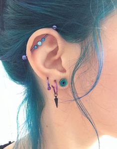 a woman with blue hair wearing ear piercings and an earring made out of beads