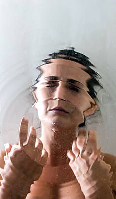 the reflection of a man's face in water with his hands on his chest