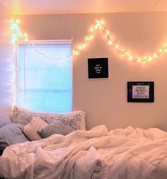 there is a bed with white sheets and lights on the wall above it in this bedroom