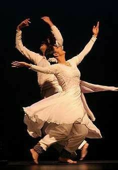 two people are dancing on stage with their arms in the air and one is wearing a white dress