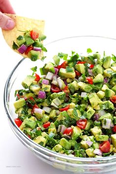 a person holding a tortilla chip over a salad