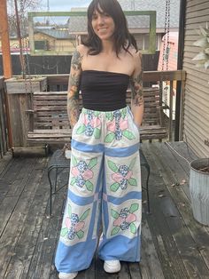 a woman standing on a porch with her hands in her pockets and wearing colorful pants