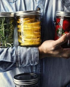 a man holding two jars filled with different types of vegetables and fruit in each jar