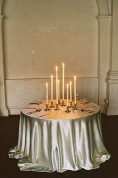 a table topped with lots of candles on top of a white cloth covered round table