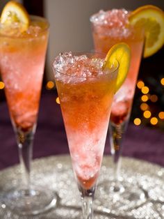 three cocktail glasses filled with pink liquid and lemon wedges on a silver platter