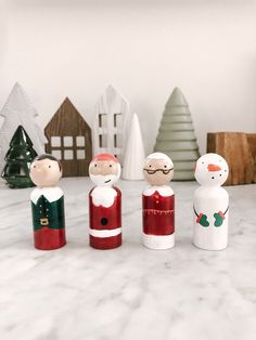 three wooden dolls are standing next to each other in front of christmas trees and small houses