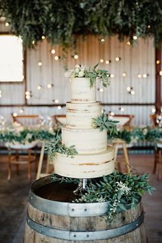 a wedding cake sitting on top of a wooden barrel in front of tables and chairs