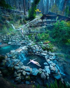 there is a man swimming in the water near some rocks and trees with stairs leading up to it