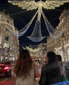 two women are walking down the street with christmas lights hanging from the ceiling above them