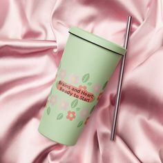 a green cup with a straw in it on a pink satin surface