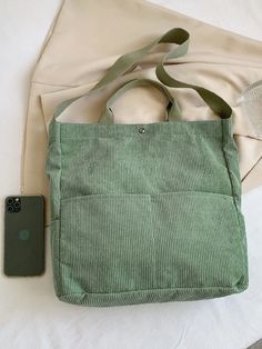 a green bag sitting on top of a bed next to an iphone