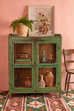 a green cabinet with some vases on top of it next to a chair and potted plant