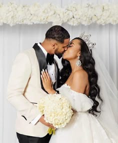 a bride and groom kissing in front of a white backdrop at their wedding ceremony,