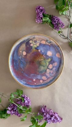 a plate with purple flowers and green leaves next to it on a tableclothed surface