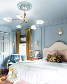 a bedroom with blue walls and white bedding, gold accents on the headboard