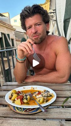 a shirtless man sitting at an outdoor table with a plate of food in front of him