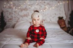 a baby sitting on top of a bed wearing a red and black checkered outfit