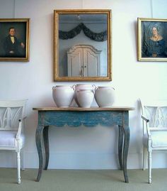 three white vases sitting on top of a blue table in front of two paintings