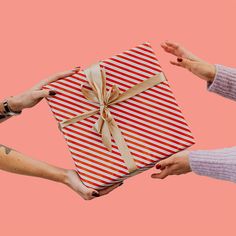 two hands holding a wrapped gift box with a ribbon on it against a pink background