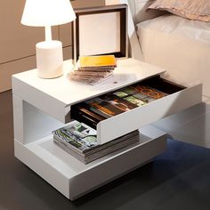 a white table with magazines in it and a lamp on the nightstand next to it