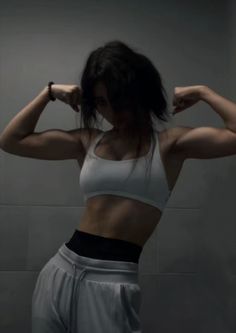 a woman in white top and grey pants flexing her muscles