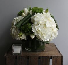 a vase filled with white flowers sitting on top of a wooden table next to a candle