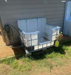 an empty trailer sitting in the grass next to a house with a hose attached to it