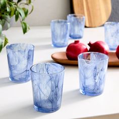 blue marbled glass cups and glasses on a white table with apples in the background