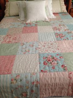 a bed with pink and blue quilts on it's headboard in a bedroom