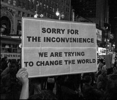 a protest sign in the middle of a crowded street with people holding up signs that read sorry for the inconvenience we are trying to change the world