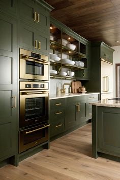 a large kitchen with green cabinets and gold trim on the oven, counter tops and drawers