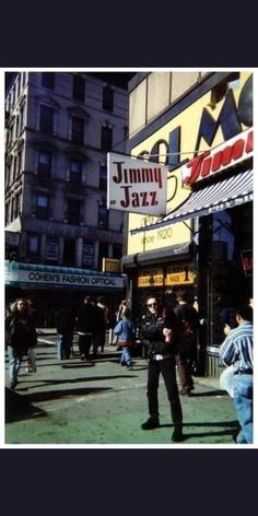 a man standing on the sidewalk in front of a jazz bar with people walking by