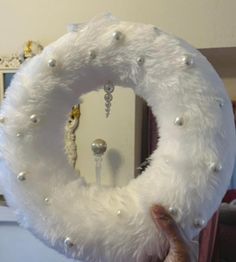 a person holding up a white wreath with pearls and beads on it in front of a mirror