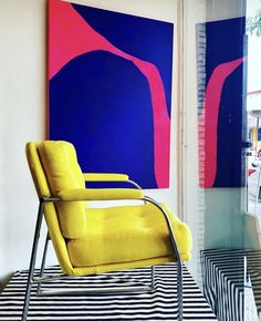 a yellow chair sitting in front of a blue and pink painting on the wall next to a black and white striped rug