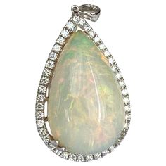 Presenting a beautiful 18.22ct white opal play of colors hand made pendant in 18 Karat white gold is a luxurious and elegant piece of jewelry. The opal, with its milky white body tone, highlights a mesmerizing play-of-color with vibrant flashes of gold, green, orange , and blue. The pendant is further adorned with 42 brilliant-cut diamonds, each of a color grade of E/F /VVS/VS clarity. The total carat weight of the diamonds is 0.72 carats, contributing to the overall brilliance and glamour of the pendant. GEM report is available. Measurements: 40x 24 mm Weight: 9.60 gr Tone Highlights, Boulder Opal Necklace, Boulder Opal Pendant, Diamond Pendant Sets, Opal Pendant Necklace, White Gold Necklaces, Modern Necklaces, Milky White, Diamond Pendant Necklace