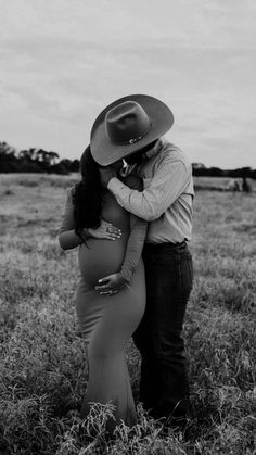 a pregnant woman hugging her husband in the middle of a field