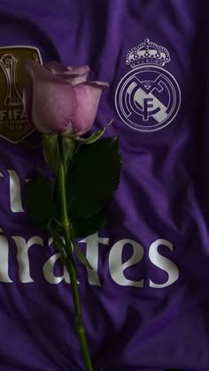 a single pink rose sitting on top of a purple soccer jersey with the real madrid logo