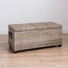 a wicker storage box sitting on top of a hard wood floor next to a white wall