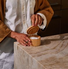 a person standing at a counter with a wooden container on it's side and one hand in the lid