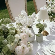 the table is set with white and pink flowers in vases, plates and silverware