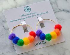 a pair of hoop earrings with multi colored pom - poms on top of it