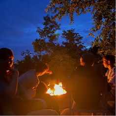 people sitting around a campfire at night with one person holding something in his hand