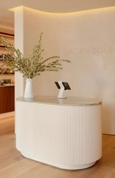 a white reception table with two vases on it and a plant in the middle