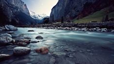 a river flowing between two mountains with rocks in the foreground and snow capped peaks in the background