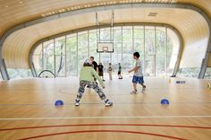 two young boys are playing basketball in an indoor gym with wooden floors and large windows