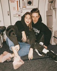 a man and woman sitting on the floor in front of a refrigerator with their arms around each other