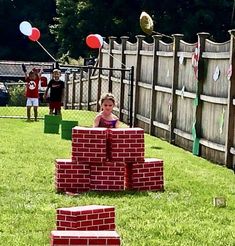 a little boy is playing in the yard with some bricks and balloons on the grass